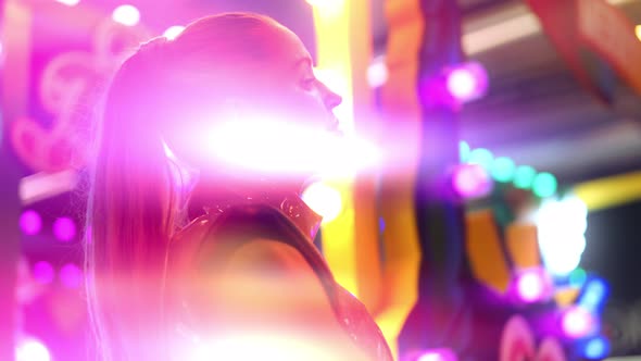 Woman In Pvc Clubwear Posing Amongst Neon Fairground Lights