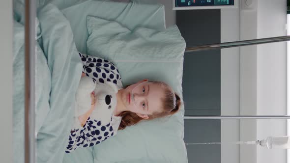 Vertical Video Portrait of Hospitalized Sick Girl Child Patient Holding Teddy Bear Resting in Bed