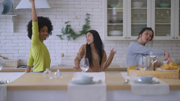 Three Carefree Cheerful Multinational Women Having Fun Dancing in Kitchen Indoors