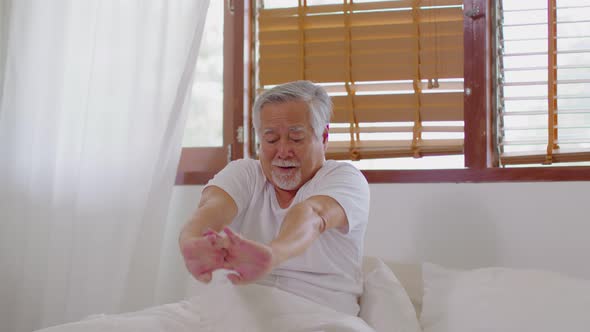 Happy Asian retirement wake up and stretching his arms in the morning so fresh and comfortable