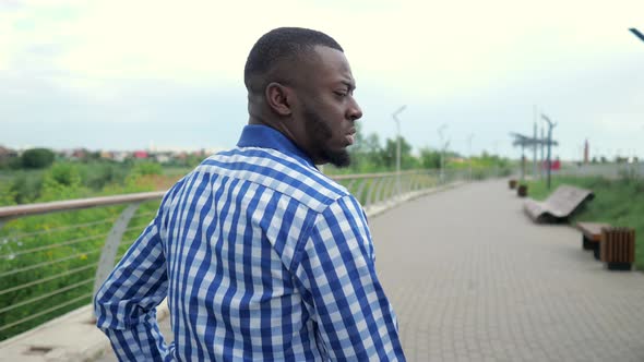 Young Afro American Man Walks in City Park Turns His Head and Smiles at Camera