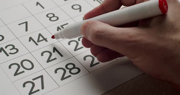 Man's Hand Write Down the 21Th Day on the Paper Calendar Using a Red Pen