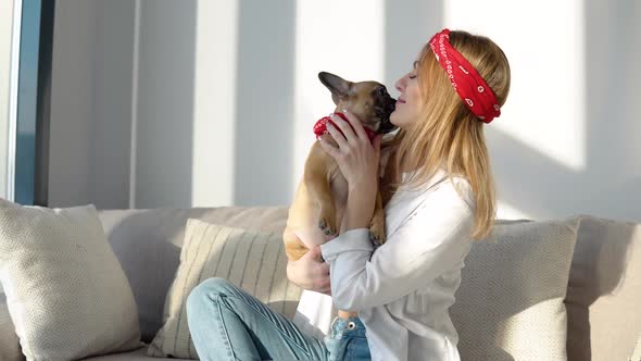 Young Woman in a White Shirt and Jeans Sits on the Sofa and Playing with Her Dog