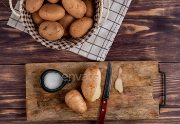 top view of potatoes with shell, knife and salt on cutting board with other ones in basket on cloth / Photodune, Misc