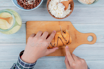 top view of male hands cutting roll with knife on cutting board with condensed milk, cottage cheese / Photodune, Misc