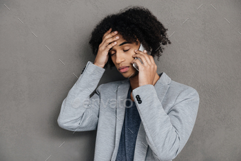 mobile phone and holding hand in hair while standing against grey background