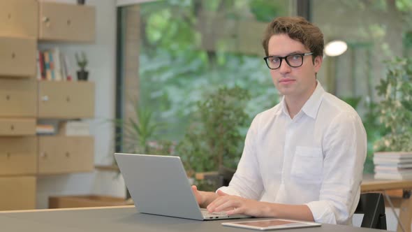 Young Man Showing Thumbs Down Sign While Using Laptop at Work