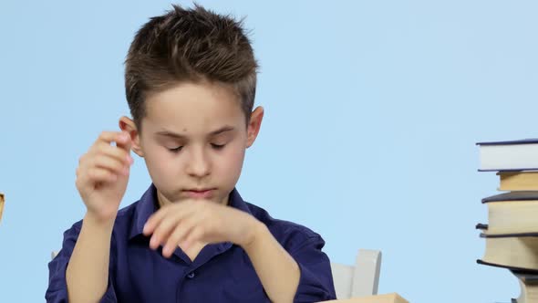 Tired Boy Sitting at a Table for a Book Falls Asleep and Wakes Up. Blue Background. Close Up