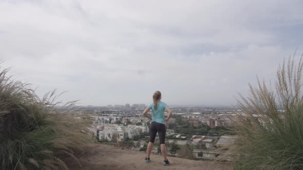 A young woman runner standing at the top of trail overlooking neighborhood.