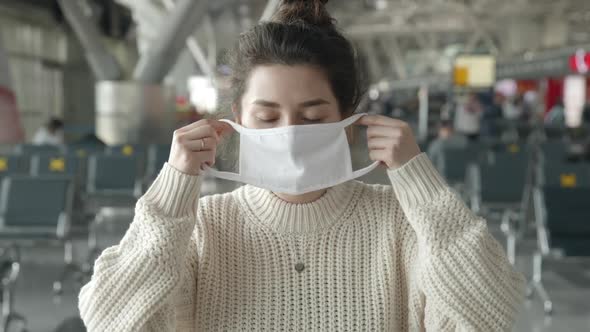 Portrait of a Woman Putting on Medical Mask Looking Straight at Camera in Airport Terminal