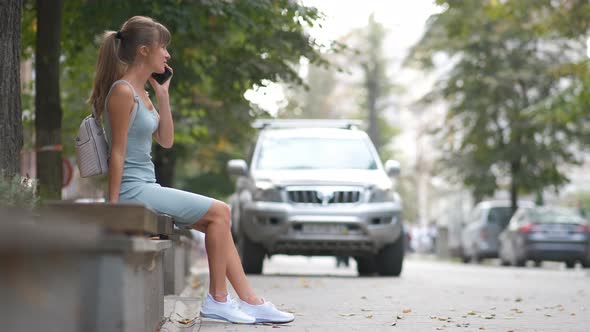 Young Pretty Woman Sitting on a Street Bench Talking on Her Smartphone Outdoors on Warm Summer Day