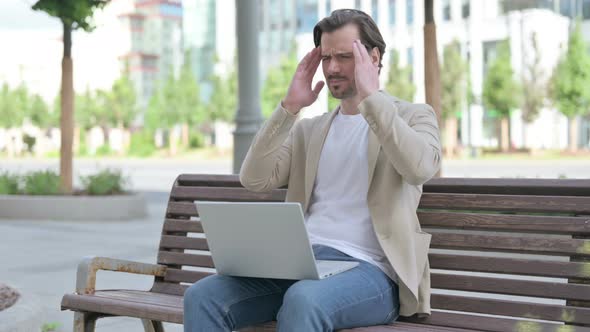 Young Man with Headache Using Laptop While Sitting on Bench