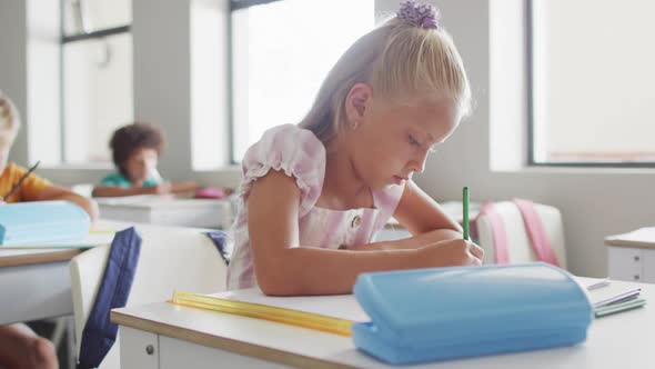 Video of focused caucasian girl sitting at desk in classsroom