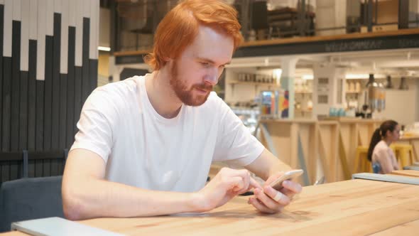 Redhead Man Typing Message on Smartphone in Cafe, Browsing