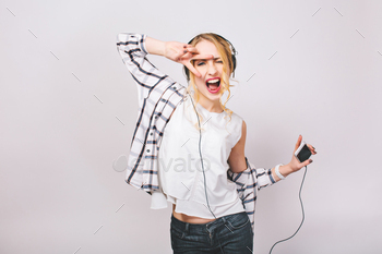 e hair in casual outfit listening to music with big headphones. She is dancing and holding smartphone. Isolated.