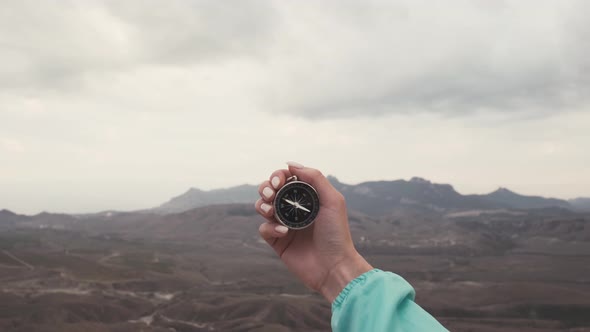 Female Hand with a Compass in Front of Mountains