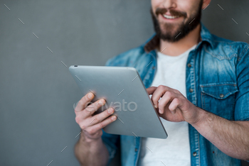  man holding digital tablet and smiling while standing against grey background