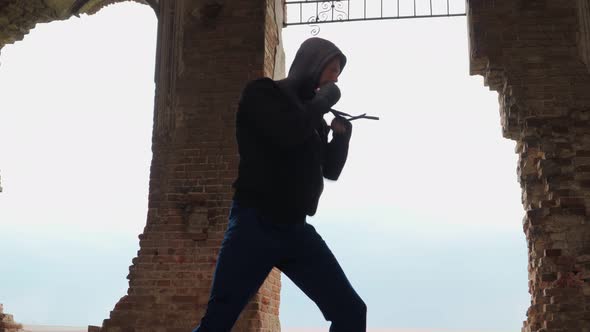 Man boxer in the hood trains beats in an abandoned building. Shadow Boxing. Outdoor workout.