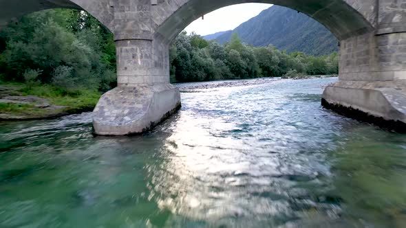 Flying under the bridge over Soca river surrounded by mountains
