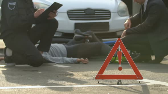 Male Policeman Filling Accident Report, Dead Female Bicyclist Lying on Asphalt