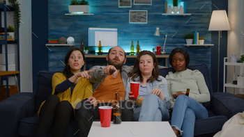 Multi-ethnic friends changing channel using remote on television