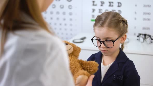 Kind Optician Giving Teddy Bear to Upset Child Patient, Psychological Help