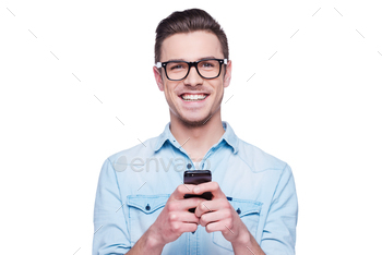 n shirt looking at camera and holding mobile phone while standing against white background