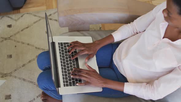 Happy african american woman sitting on armchair in living room, using laptop