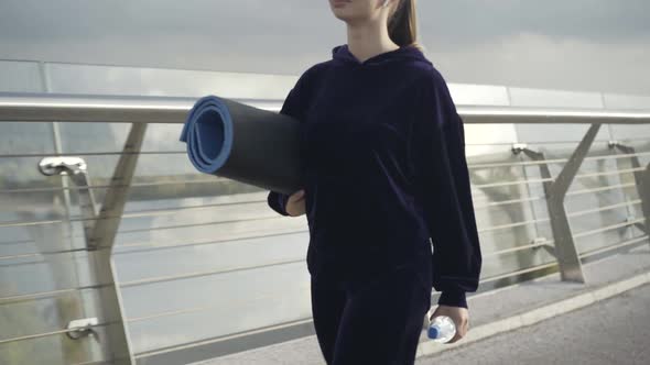 Unrecognizable Fit Confident Sportswoman Walking with Water Bottle and Rolled Exercise Mat