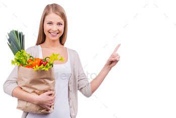 g a shopping bag full of groceries and pointing away while standing against white background