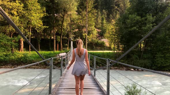 This 4k clip shows a beautiful girl walking across a little cable bridge in slovenia.  Under the bri