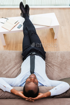 man in formalwear lying on the couch with his legs on a desk and hands behind head