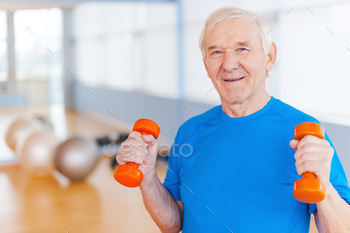 ng with dumbbells and smiling while standing indoors