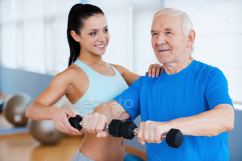 cal therapist helping senior man with fitness in health club