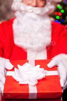 g out a gift box and smiling with Christmas Tree in the background