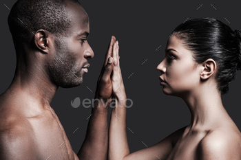 can man and Caucasian woman holding their hands clasped and looking at camera while standing against grey background