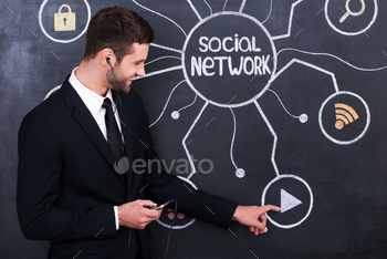 n headphones holding telephone while standing against social network chalk drawing on blackboard