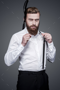 sting his suspenders and keeping eyes closed while standing against grey background