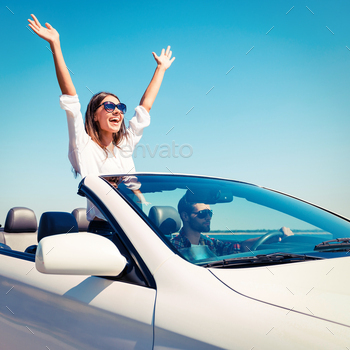  road trip in their convertible while woman raising arms and smiling