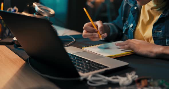 Closeup of Girl's Hands Taking Notes with Pencil in Notebook Laptop Headphones Teenage Girl Has