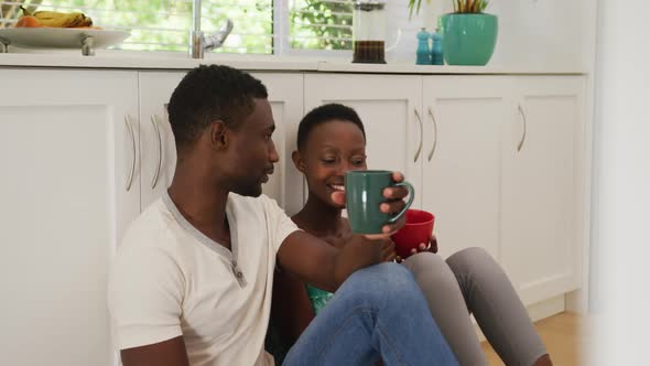 African american couple sitting on kitchen floor drinking coffee and talking