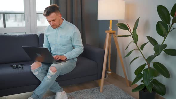 Man with Glasses Sitting on the Sofa with Laptop and Working in Cozy Room