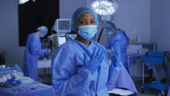 African american female surgeon wearing face mask and protective clothing in operating theatre