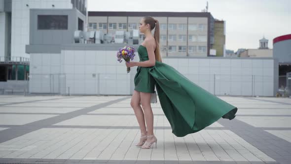 Beautiful Girl in Chic Dress Walking with Fragrant Bouquet of Wildflowers on the Background