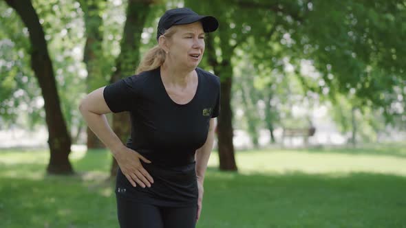 Middle Shot of Mid-adult Woman Suffering Stomach Cramps After Jogging in Summer Park. Portrait of