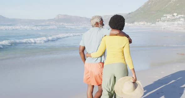 Happy african american couple walking and embracing on sunny beach