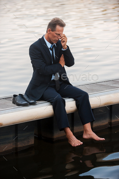 g his face with hand while sitting barefoot at the quayside