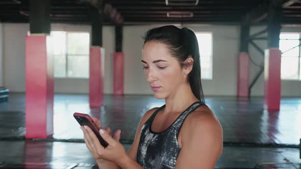 Woman Using Smart Phone with Personal Trainer Workout App in Gym