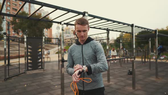 Young Sportsman Checking Heart Rate on Sports Watch During Exercise Jumping on Rolling Pin at Street