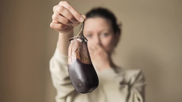 Young Woman Picks Up an Old Moldy Eggplant and Covers Her Nose From the Unpleasant Smell